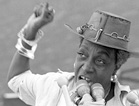 Activist Flo Kennedy with raised right arm, speaks into a bank of microphones to a crowd out of view