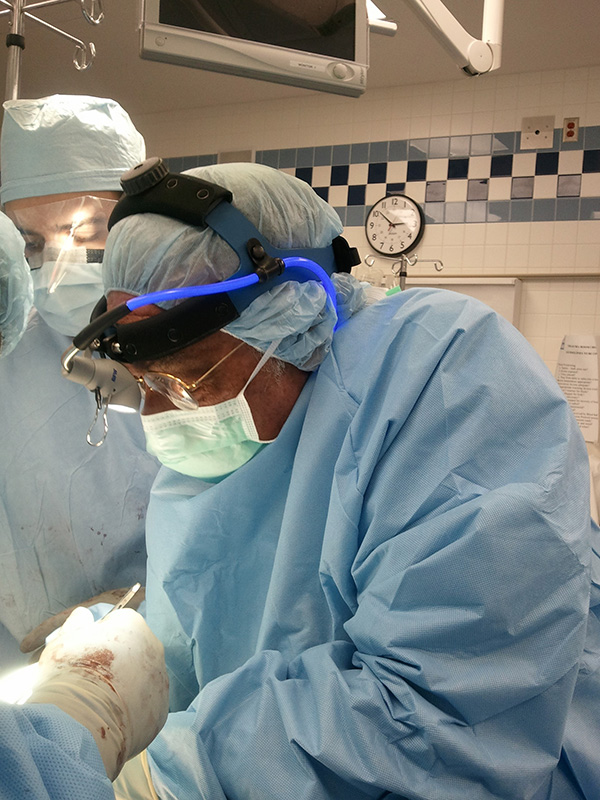 Left profile of a surgeon in scrubs preforming an operation.