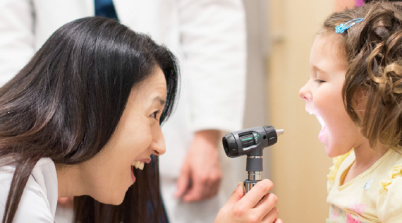 Asian woman smiles while looking into a White girl's mouth.