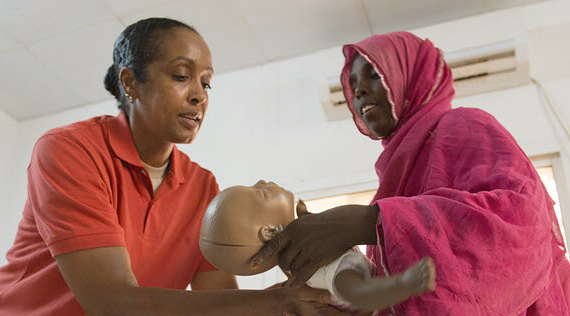 African America woman hands an infant sized mannequin to an African woman.